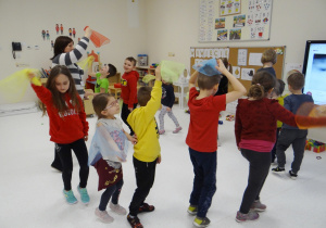 Dzieci tańczą z panią w kole, trzymając kolorowe chustki.